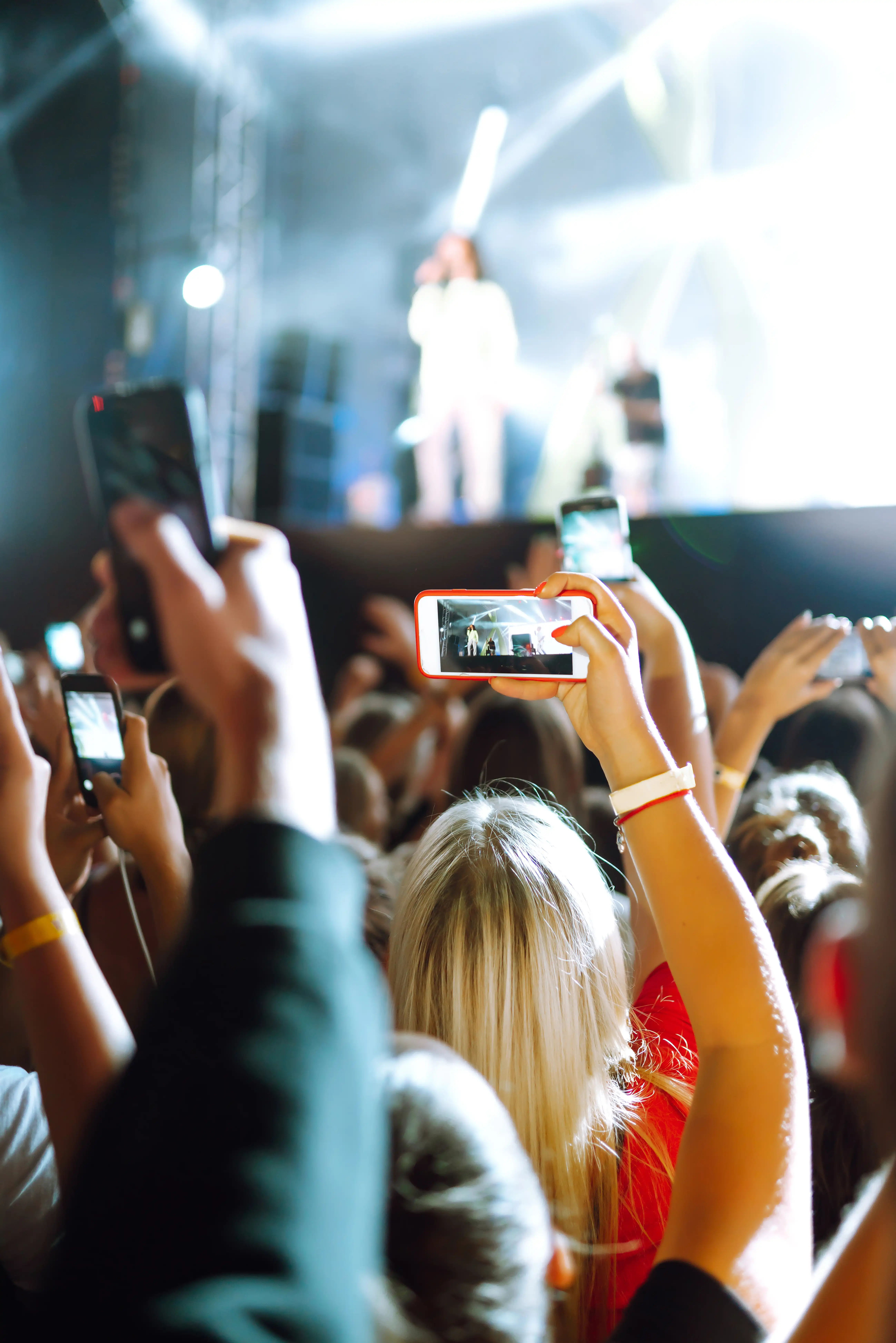 Menschen, die während eines Musikfestivals mit ihrem Smartphone Fotos machen. Fans, die ein Rockkonzert mit Lichtshow genießen und in die Hände klatschen.